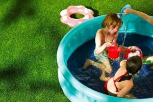 drie kinderen die aan het spelen zijn in een zwembadje die staat op het kunstgras aangelegd door het kunstgrascentrum.