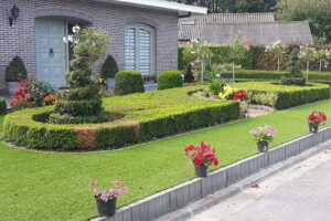 Een prachtige voortuin met kunstgras aangelegd door het kunstgrascentrum rond ovaal vormige beplanting in het midden.
