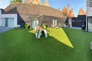Kunstgras geplaats door het kunstgrascentrum op het dak van Brugse B&B waarbij een barbecue, een bank, stoeltjes en nog meer op het kunstgras staat.