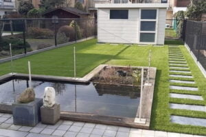 Een foto van een tuin die geplaatst werd met kunstgras door het kunstgrascentrum met de kunstgrassoort sense rondom stapstenen en vijver.