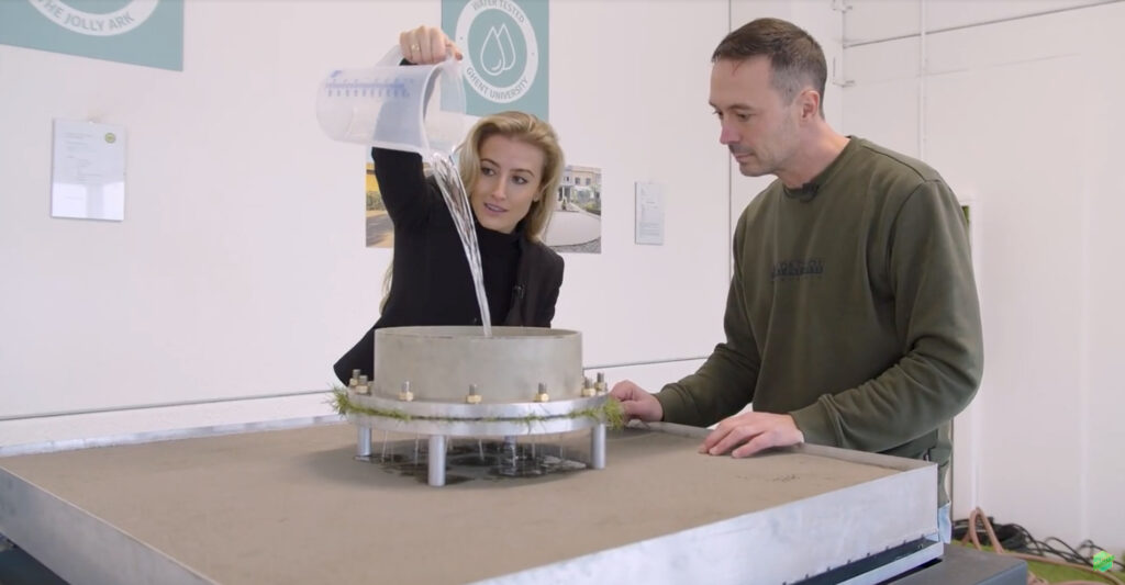 Dame van ESTC en Man van Laboratorium Universiteit gent gieten water door het licht gebonden zand voor de waterdoorlaatbaarheid te testen van de ondergrond voor kunstgras.