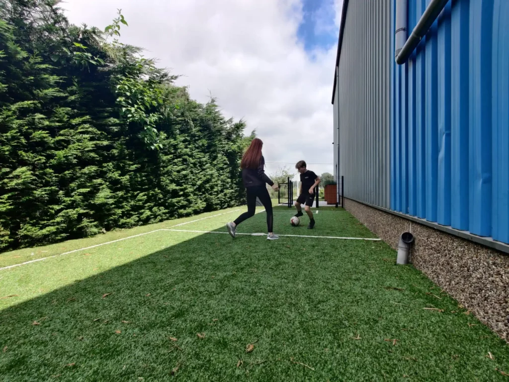 Twee mensen die aan het voetballen zijn op een sportveldje die is aangelegd met kunstgras door het kunstgrascentrum.