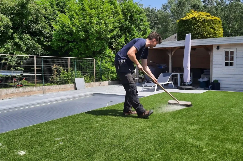 Een werkman van het kunstgrascentrum is bezig met het zand handmatig in het kunstgras te borstelen